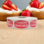 Strawberry cream cheese sticker with red background and white letters on a roll of labels