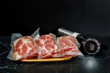 Sous Vide Cooker Immersion Circulator and meat on a dark background.